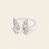 A silver butterfly ring set with clear pavé stones, displayed on a clean, solid cream-colored background.
