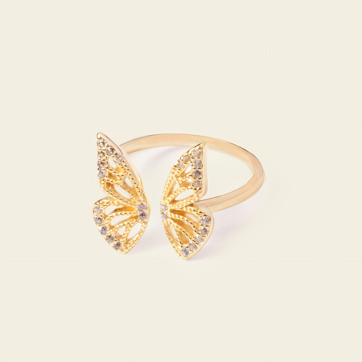 Gold butterfly-shaped ring with gemstones on a beige background