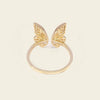 A gold plated butterfly ring with two delicate wing motifs on a smooth band, set against a solid light beige background.