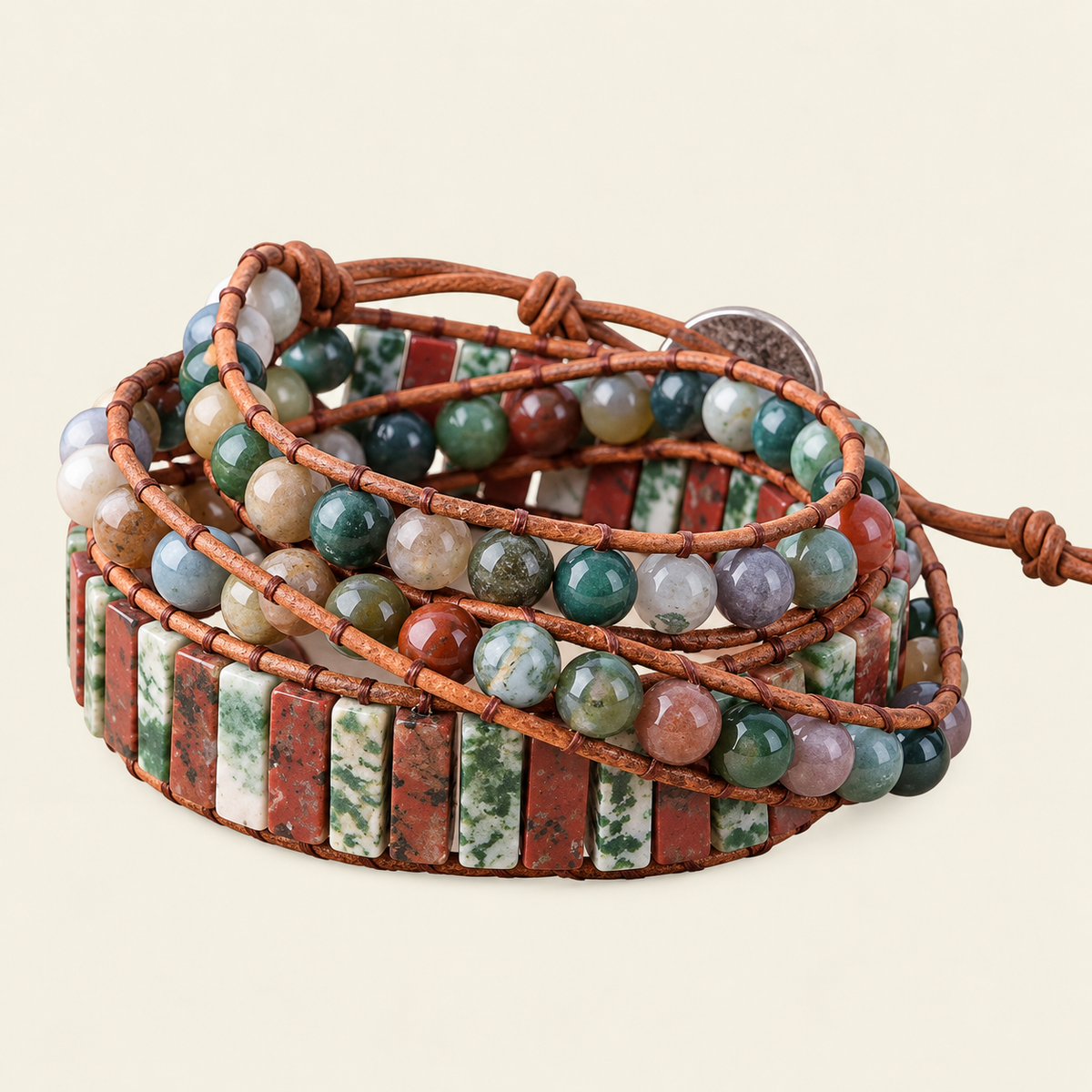 A multi-strand wrap bracelet made of brown cord and polished stone beads and rectangular stone tiles in earthy red, green, white, and gray tones, photographed on a plain light beige background.