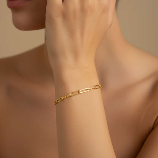 Gold chain bracelet on a wrist with a neutral background