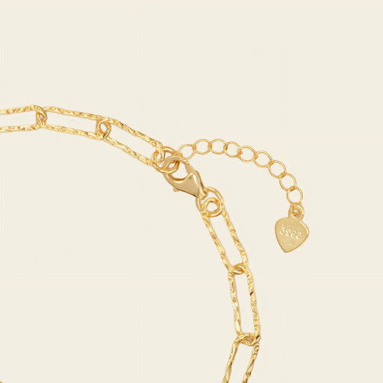 Gold chain bracelet with a heart-shaped tag on a beige background