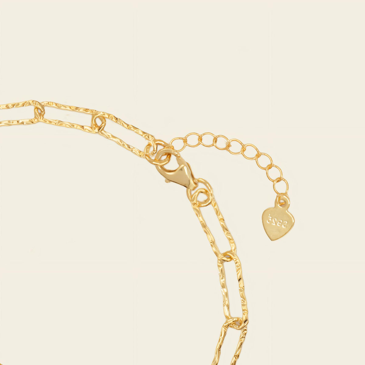 Gold chain bracelet with a heart-shaped tag on a beige background