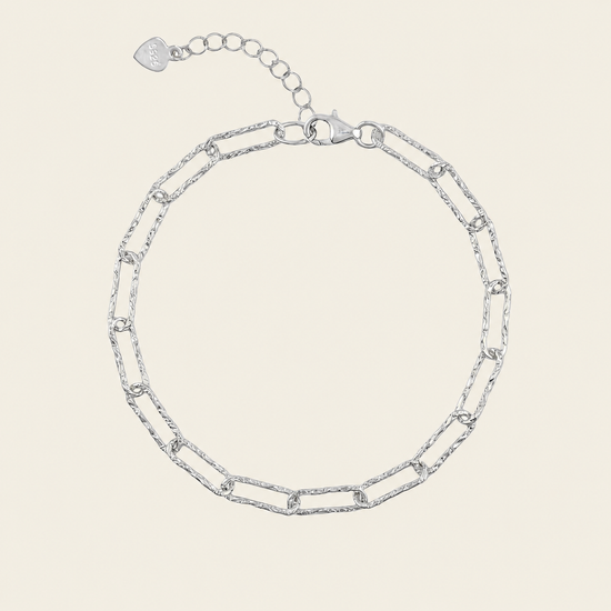 A silver chain link bracelet with elongated oval links and a lobster clasp, shown on a light beige background.