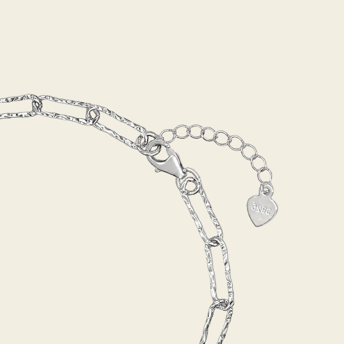 Close-up of a silver chain necklace showing a lobster clasp, extension chain, and a heart-shaped tag engraved with 'LOVE'.