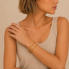 Woman wearing a beige tank top and gold bracelets on a beige background