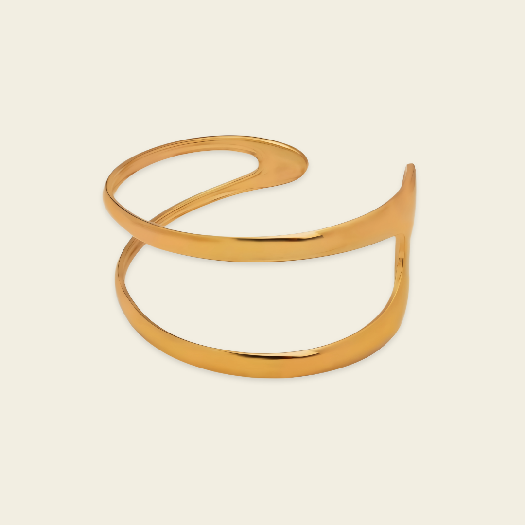 A polished gold-tone metal cuff bracelet with an organic, flowing looped design, shown on a solid light beige background.