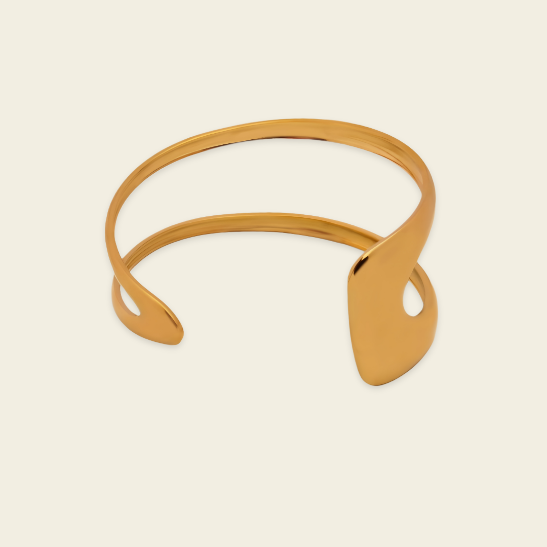 A polished gold-tone open cuff bracelet with a smooth, flowing organic design, displayed on a light cream background.