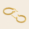 A pair of gold-toned twisted hoop earrings with leverback closures, displayed on a light cream background.