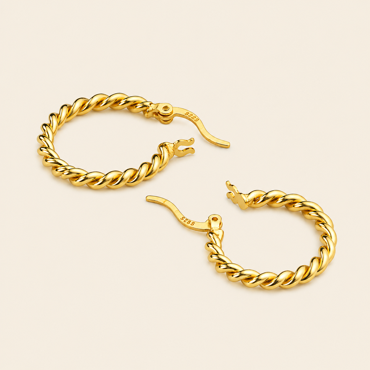 A pair of gold-toned twisted hoop earrings with leverback closures, displayed on a light cream background.