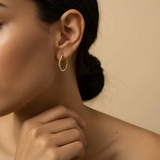 Close-up of a person wearing a gold hoop earring against a beige background