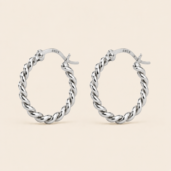 A pair of silver twisted hoop earrings with a polished finish and a '925' sterling silver hallmark on the inside, displayed against a solid light beige background.