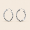 A pair of silver twisted hoop earrings with a polished finish and a '925' sterling silver hallmark on the inside, displayed against a solid light beige background.