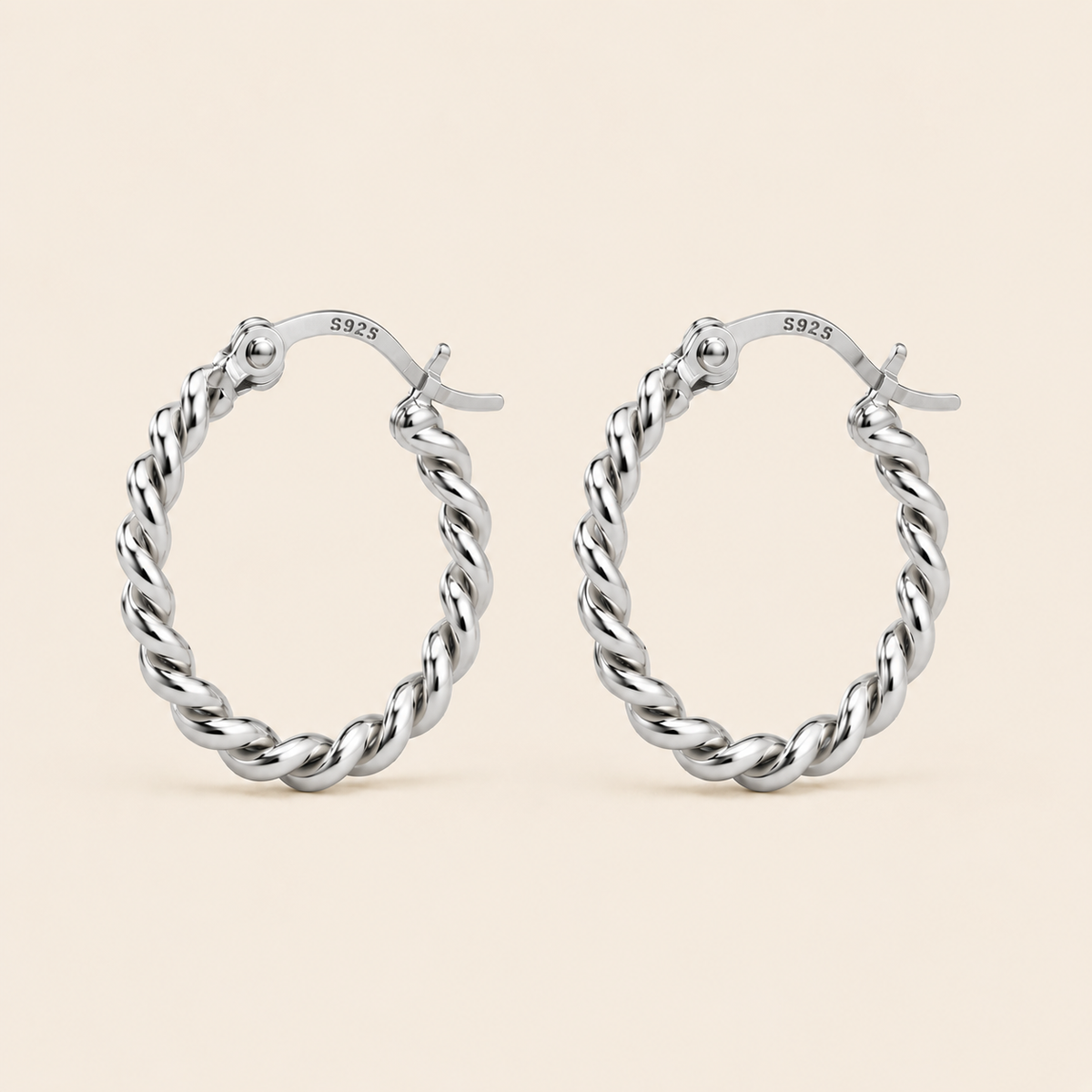 A pair of silver twisted hoop earrings with a polished finish and a '925' sterling silver hallmark on the inside, displayed against a solid light beige background.