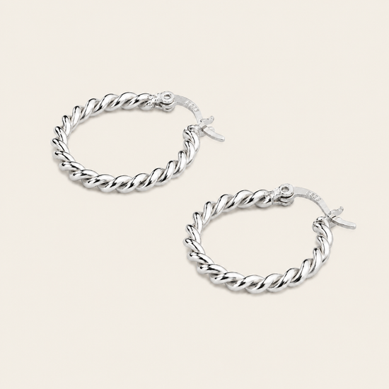 A pair of silver twisted rope hoop earrings with fishhook backings, displayed on a light beige background.