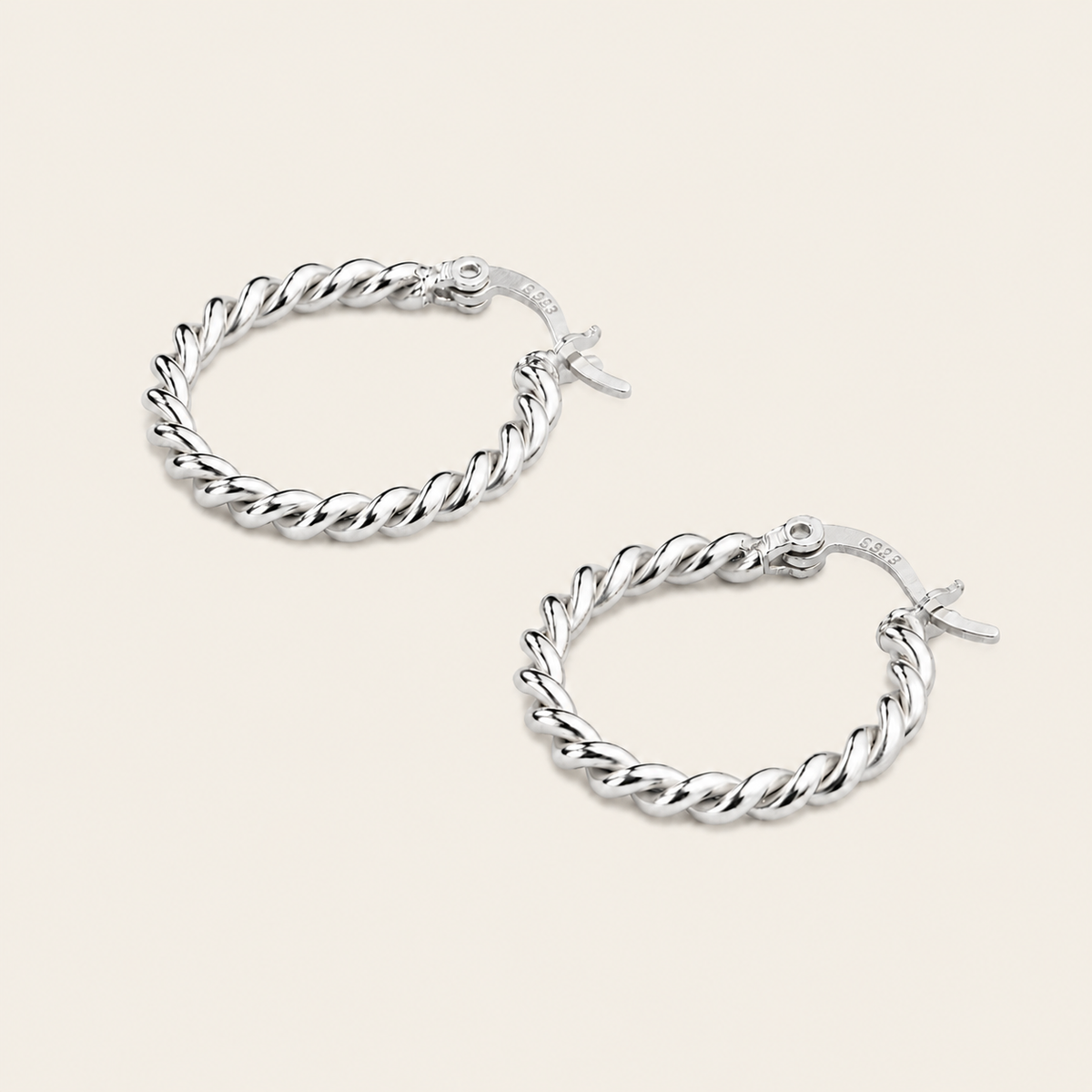 A pair of silver twisted rope hoop earrings with fishhook backings, displayed on a light beige background.