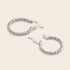 A pair of silver-toned twisted rope hoop earrings with fishhook closures, displayed on a solid light beige background.