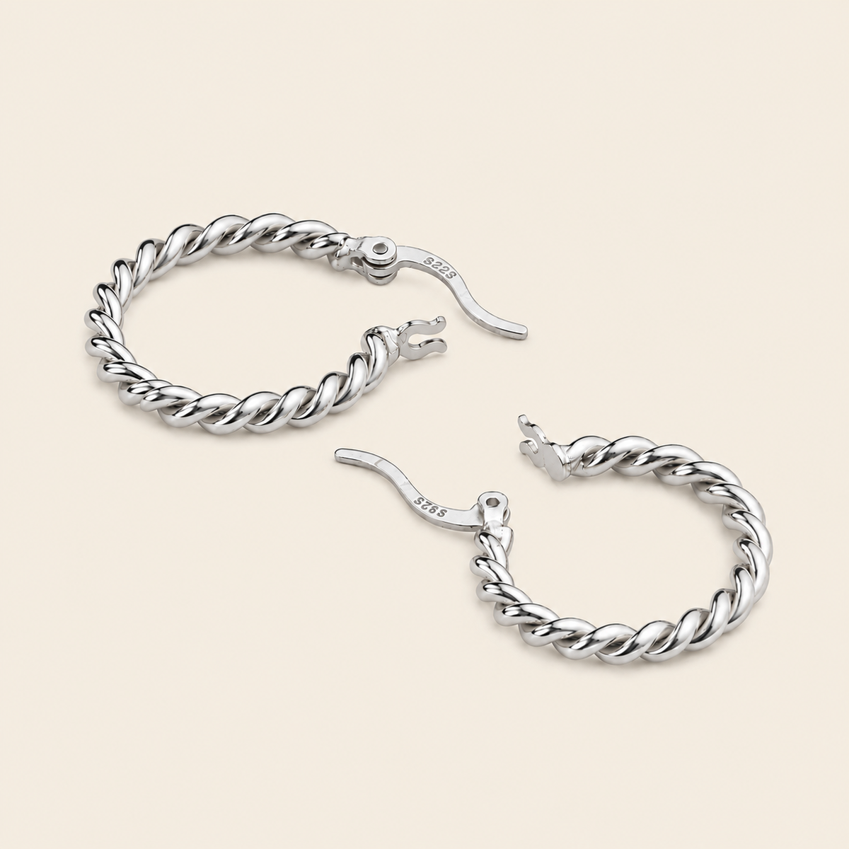 A pair of silver-toned twisted rope hoop earrings with fishhook closures, displayed on a solid light beige background.