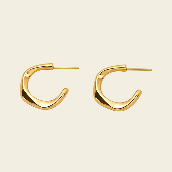 A pair of abstract, open-ended gold hoop earrings with a polished finish, displayed on a light beige background.