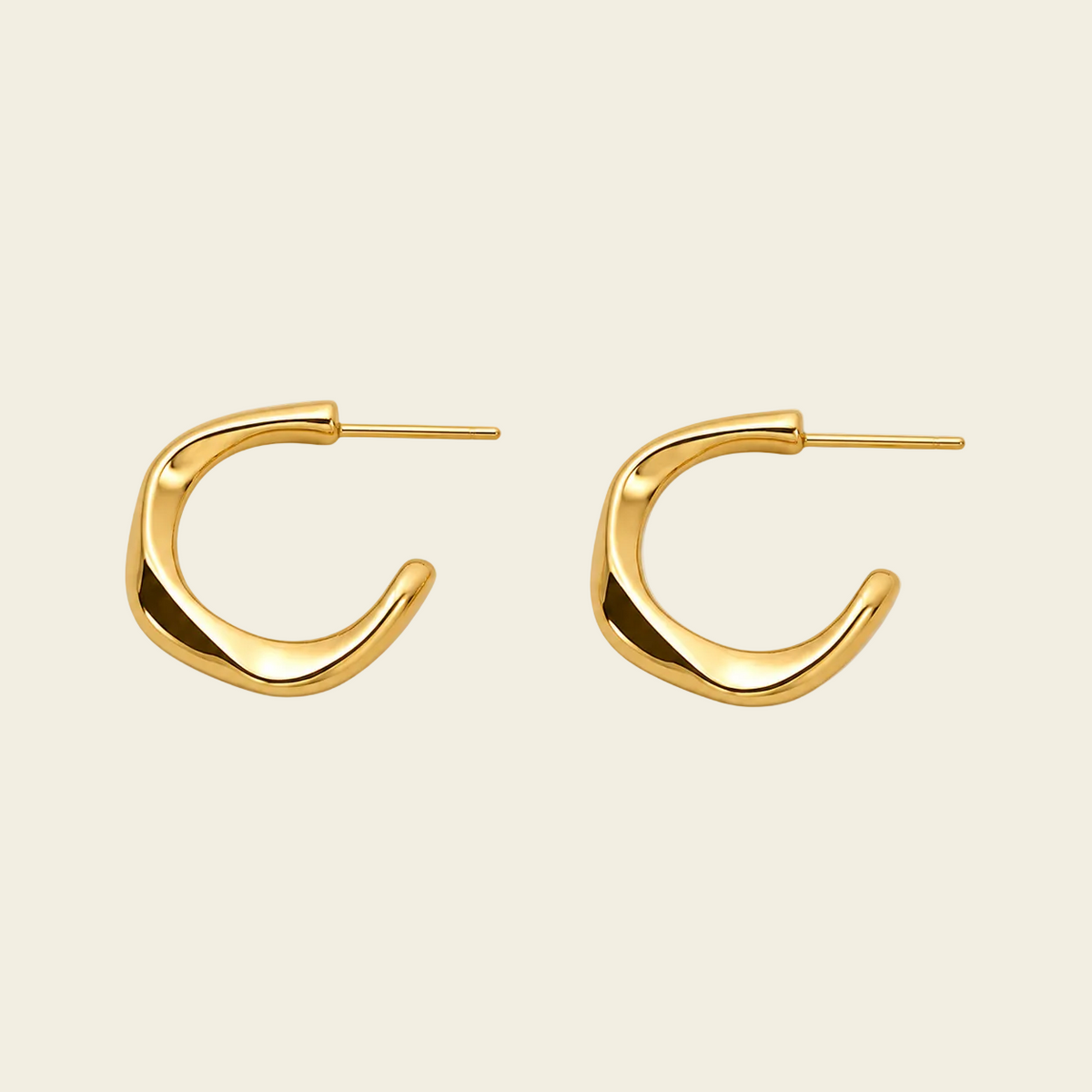 A pair of abstract, open-ended gold hoop earrings with a polished finish, displayed on a light beige background.