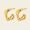 A pair of polished gold abstract hoop earrings with a curved, organic shape and post backs, displayed on a clean, solid cream background.