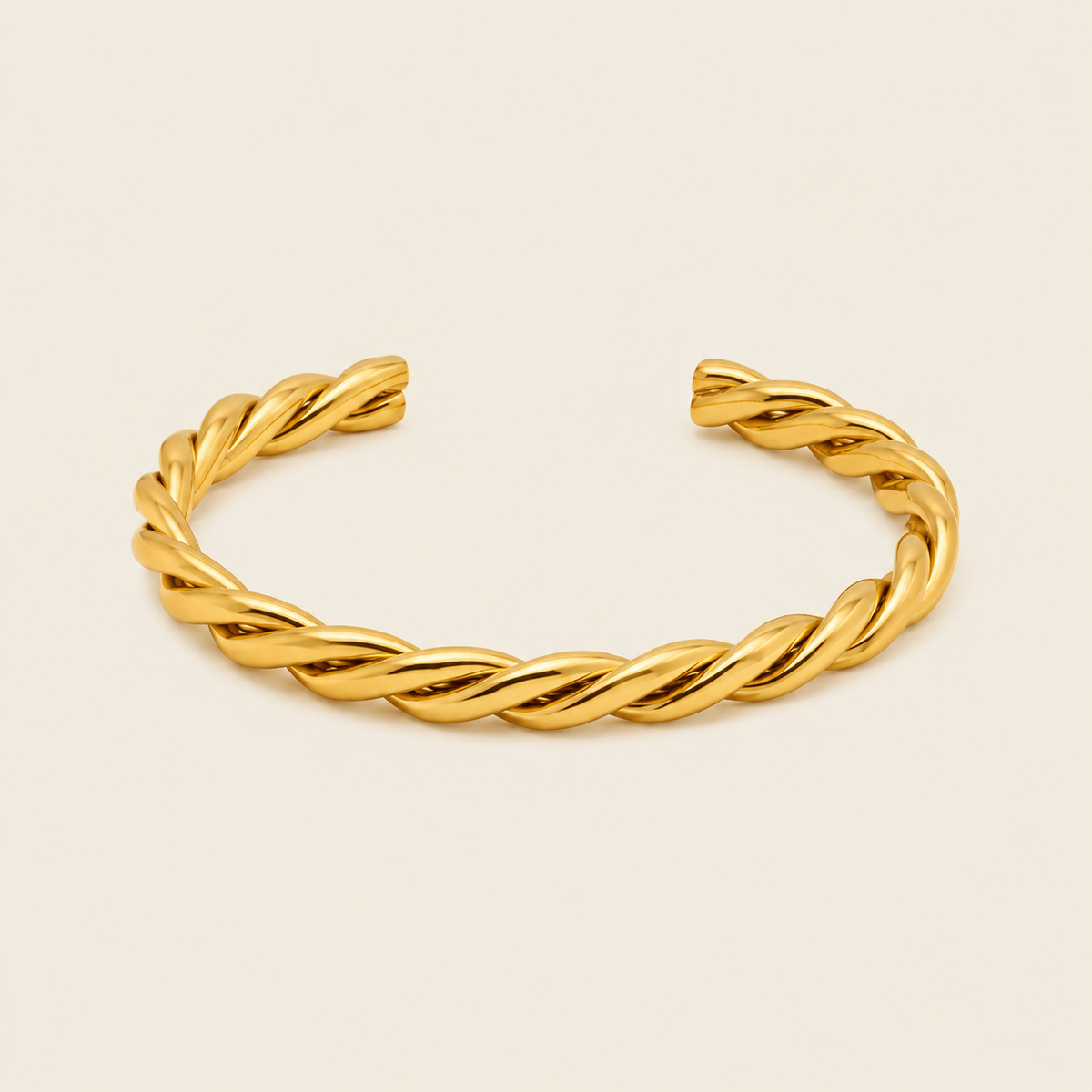 A twisted open cuff bracelet in polished yellow gold, displayed on a clean, solid, light cream background.