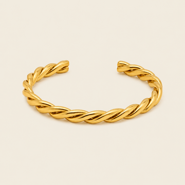 A twisted open cuff bracelet in polished yellow gold, displayed on a clean, solid, light cream background.