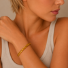 Close-up of a woman wearing a gold bracelet on a neutral background