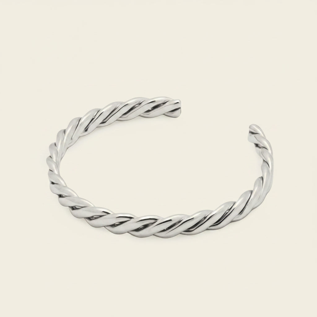 A twisted open cuff bracelet in polished silver, displayed on a solid light beige background.