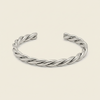A twisted open cuff bracelet in polished silver, displayed on a clean, solid, light cream background.