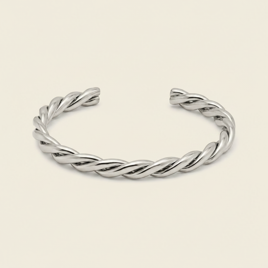 A twisted open cuff bracelet in polished silver, displayed on a clean, solid, light cream background.