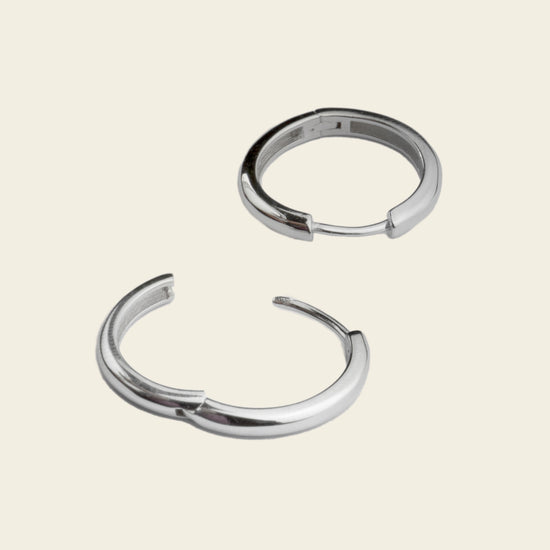 Two silver hoop earrings on a light beige background