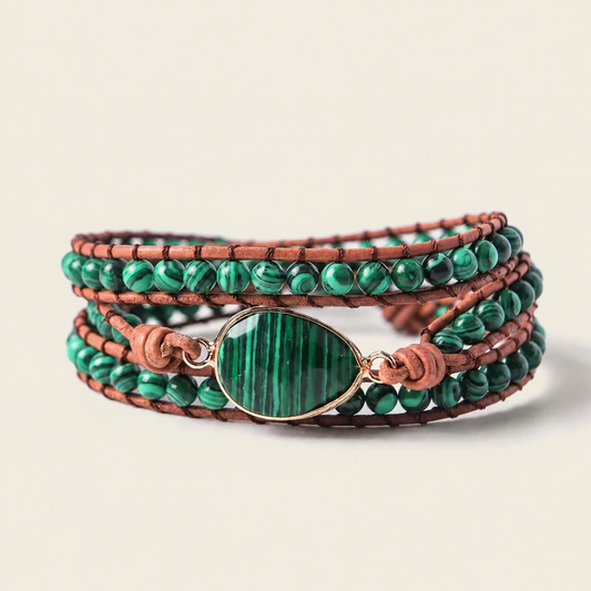 A multi-strand wrap bracelet featuring brown leather cords, green malachite beads, and a central oval green stone with a gold-toned bezel, shown on a light beige background.