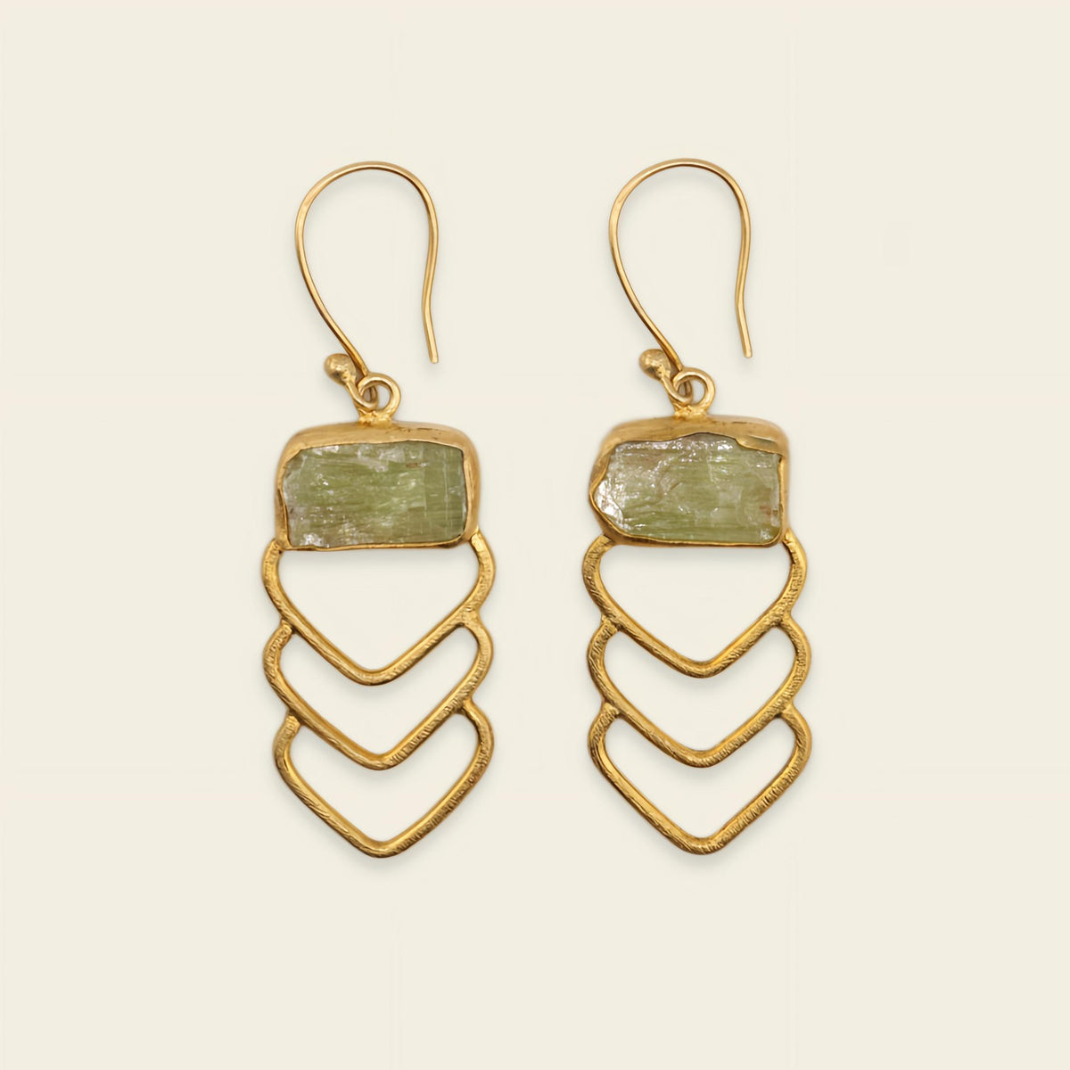 Gold earrings with green stone on a beige background