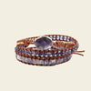 Multistrand bracelet with purple beads and a brown leather strap on a beige background