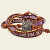 Multistrand bracelet with purple beads, brown leather, and a silver charm on a beige background