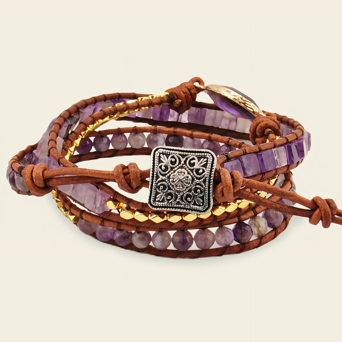 Multistrand bracelet with purple beads, brown leather, and a silver charm on a beige background