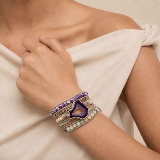 Hand wearing multiple bracelets with a neutral background