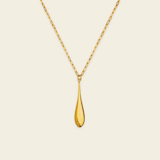 A polished gold teardrop pendant necklace on a delicate gold chain, presented against a solid, warm off-white background.