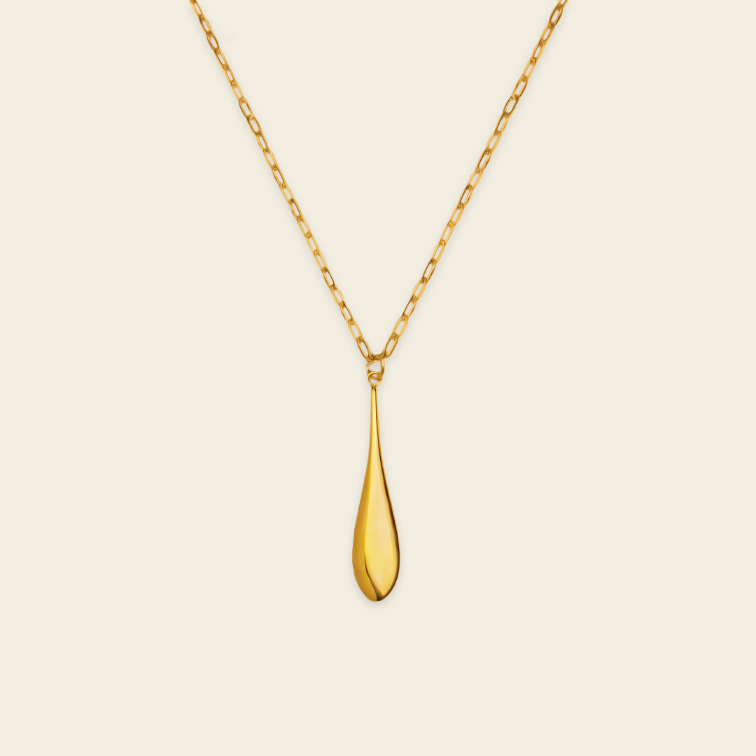 A polished gold teardrop pendant necklace on a delicate gold chain, presented against a solid, warm off-white background.