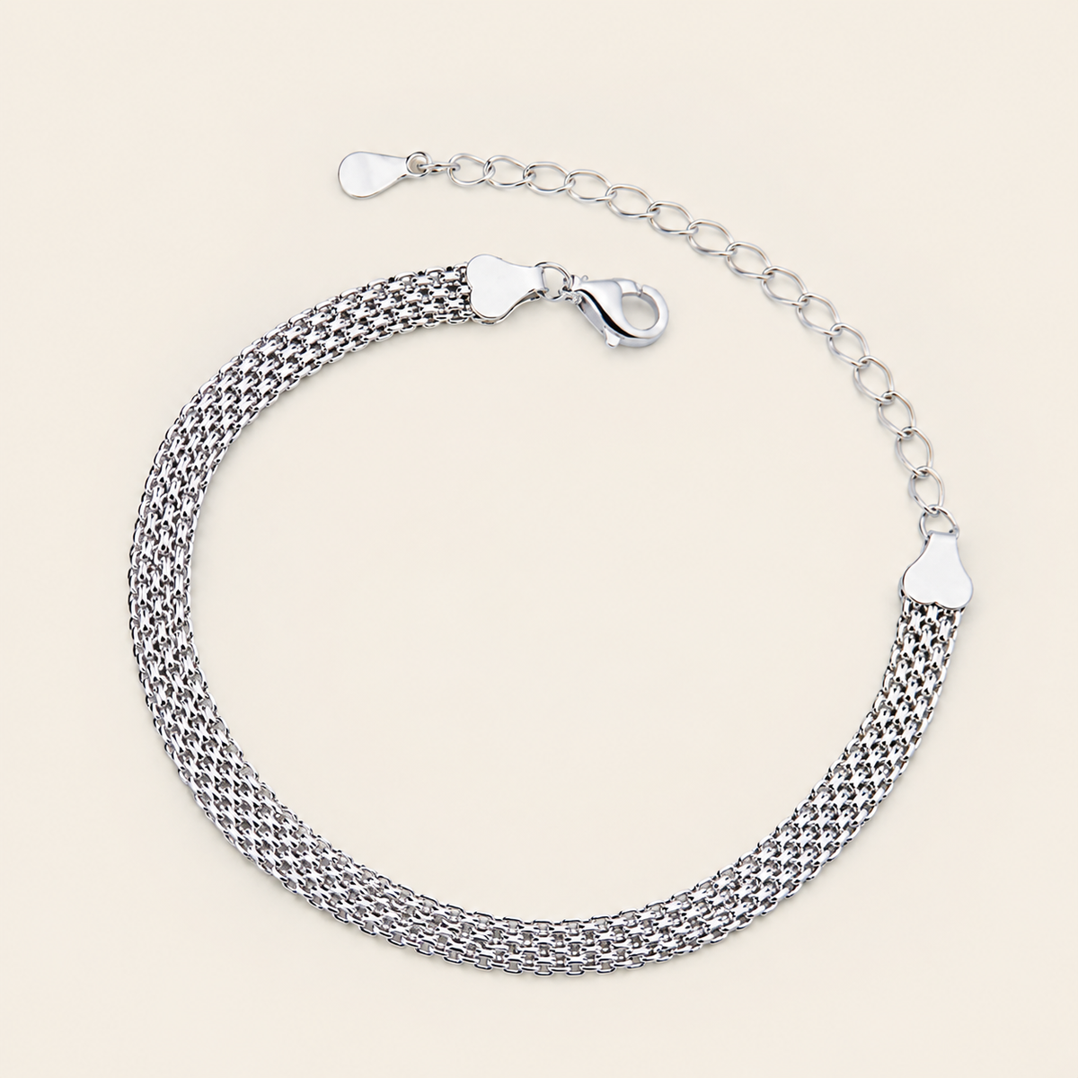 A silver mesh chain bracelet with a lobster clasp and extender chain, displayed on a light beige background.