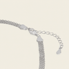 Close-up of a silver-toned chain necklace showing the clasp, extender chain, and heart-shaped tag on a light cream background.