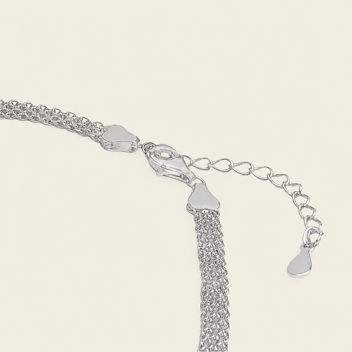 Close-up of a silver-toned chain necklace showing the clasp, extender chain, and heart-shaped tag on a light cream background.