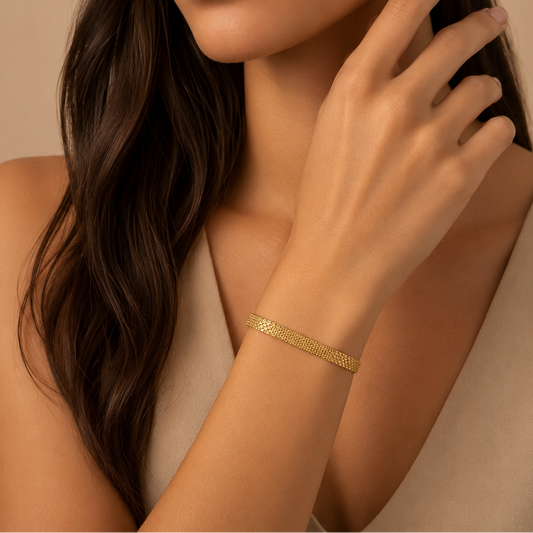 Gold bracelet on a woman's wrist with a neutral background