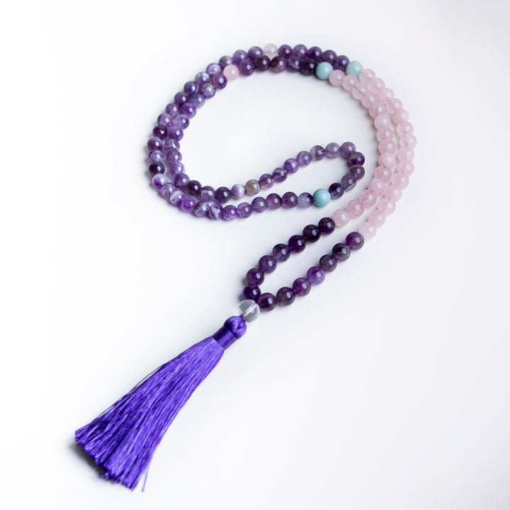Minimalist flatlay of a handmade necklace featuring amethyst and rose quartz beads with a rich purple tassel