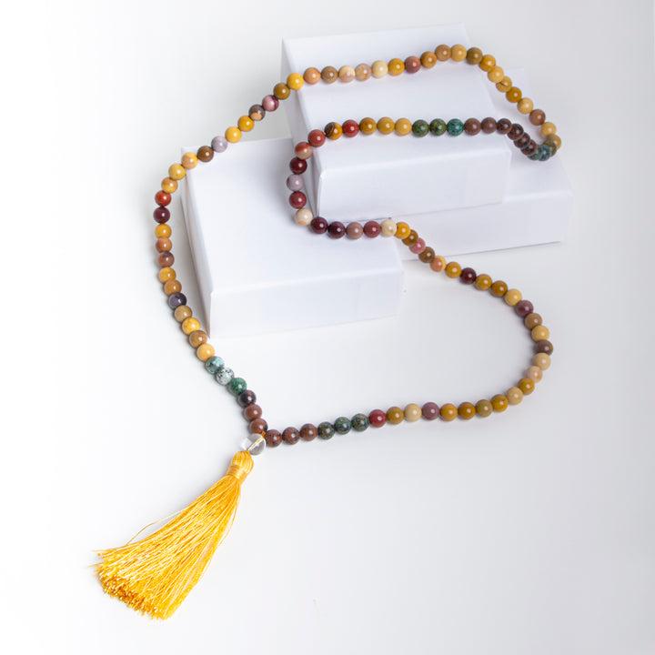 Handmade beaded necklace featuring multicoloured Jasper stones with earthy tones and a vibrant yellow tassel, styled on white boxes for a bright boho look.