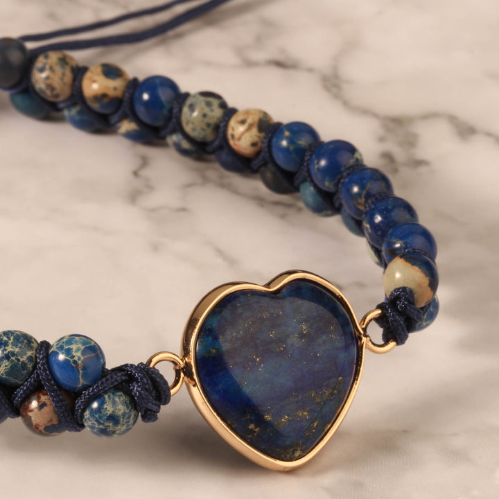 Close-up of a handmade adjustable bracelet featuring deep blue lapis lazuli stone beads and a heart-shaped lapis lazuli centerpiece, wrapped in gold-tone accents.