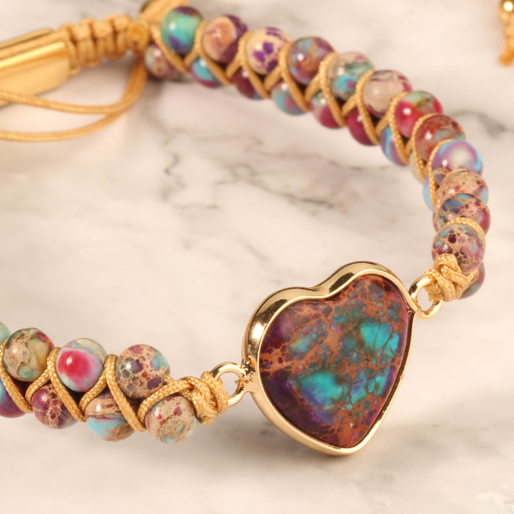 Close-up of a handmade adjustable bracelet featuring multicolored jasper stone beads and a heart-shaped jasper centerpiece, wrapped in gold-tone accents.