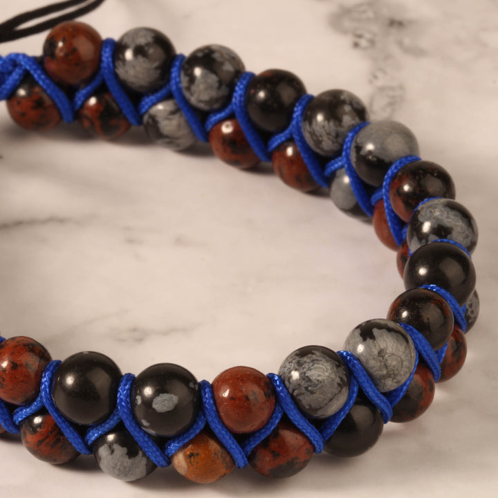 Close-up of a handmade beaded bracelet featuring natural stones in black, gray, and red hues, wrapped with vibrant blue woven cord.