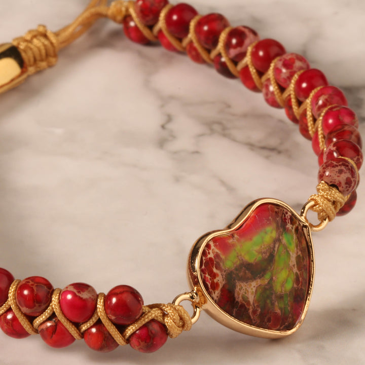 Close-up of a handmade adjustable bracelet featuring red jasper stone beads and a heart-shaped red jasper centerpiece, wrapped in gold-tone accents.
